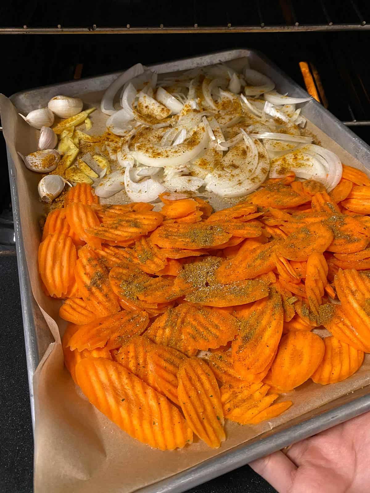 Karotten-Curry-Suppe mit Nudeln 4 Gemüse für Curry-Karotten-Suppe mit Nudeln auf einem Backblech, das in den Ofen geschoben wird