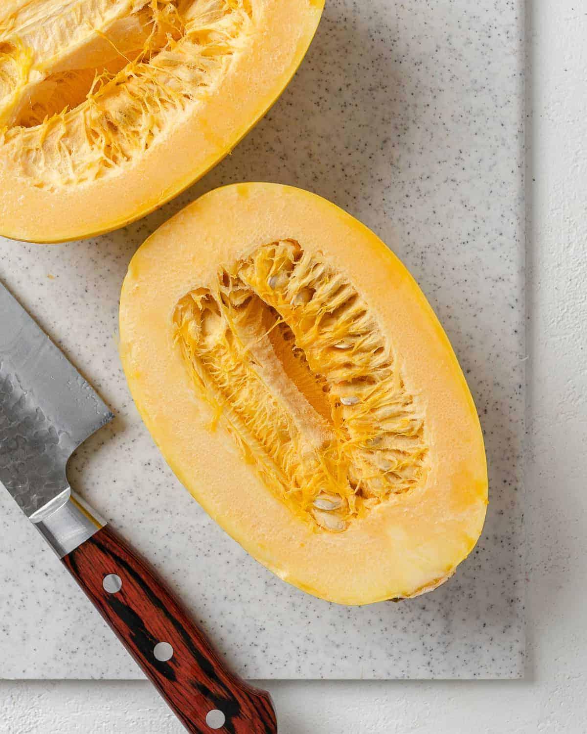 Chili-Käse-gefüllter Spaghettikürbis 4 squash cut in half against white speckled cutting baord