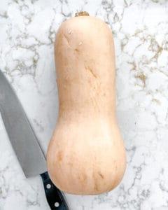 Roher Butternut-Kürbis mit Messer auf weißem Marmorhintergrund