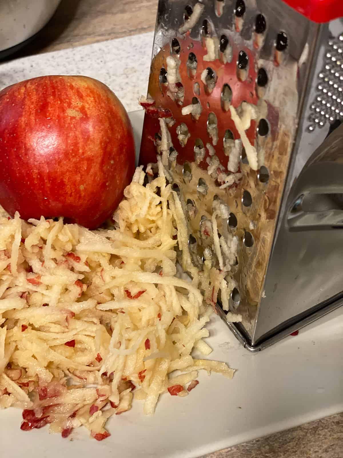 Einfache Vegane Apfelmuffins 4 Arbeitsschritt: Äpfel reiben mit Apfel im Hintergrund