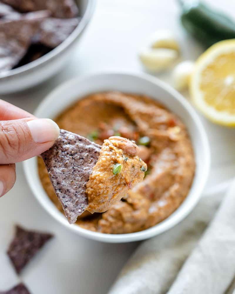 Gewürzter Bohnen-Dip 4 completed Spiced Refried Bean Dip in a bowl against a white background with ingredients spread in the back