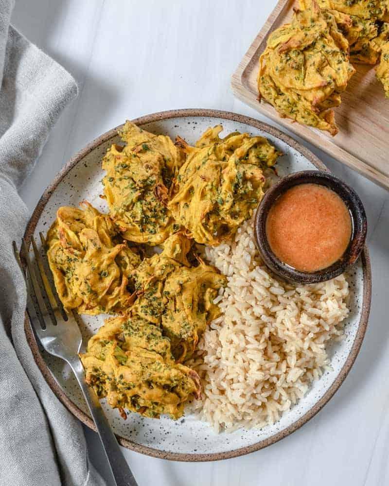 Fertige Brokkoli- und Zwiebel-Pakora auf einem Teller mit Reis und einer Sauce angerichtet