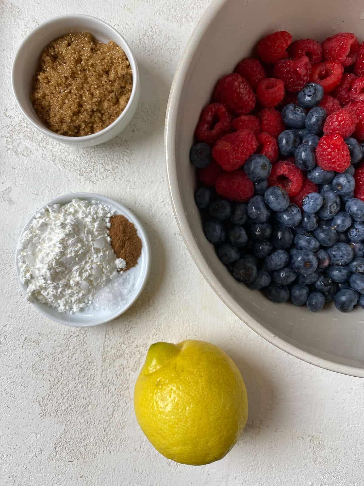 ingredients for Mixed Berry Crumb Pie measured out on a white surface alongside a bowl