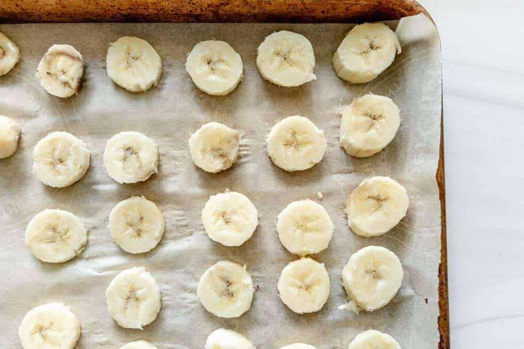 Nahaufnahme von gefrorenen Bananenscheiben auf einem mit Backpapier ausgelegten Backblech.