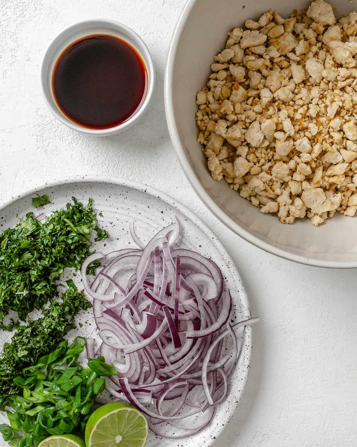 Veganer Tofu-Larb-Salat 5 Larb und Gemüse in zwei separaten weißen Schalen neben Sauce auf weißem Hintergrund.