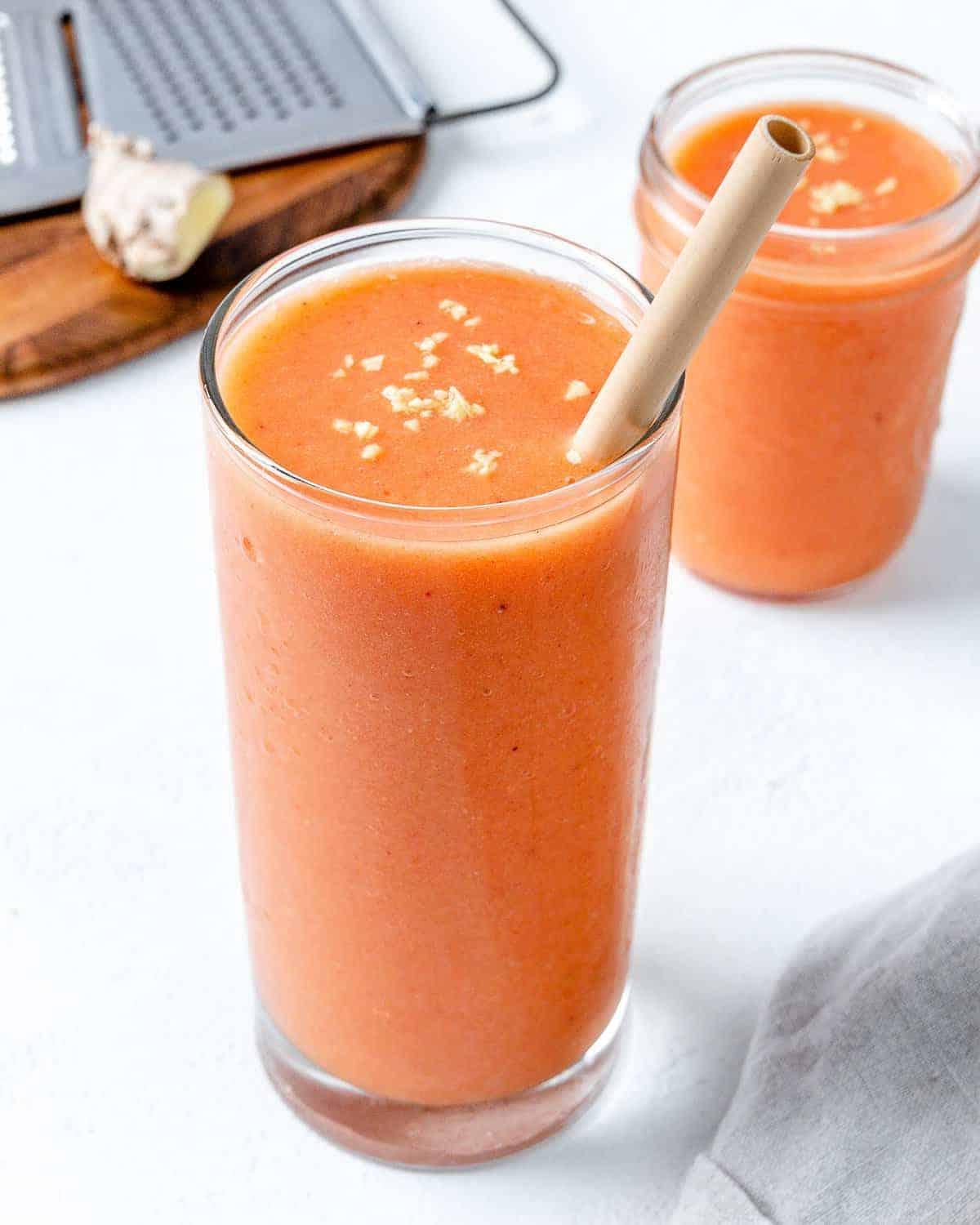 Ingwer-Frucht-Smoothie 5 Fertiger Ingwer-Frucht-Smoothie in einem hohen Glasbecher mit einem Papierstrohhalm im Vordergrund und einem kleinen Glas Smoothie im Hintergrund
