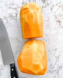 Geschälter und halbierter Butternut-Kürbis mit Messer auf weißem Marmorhintergrund