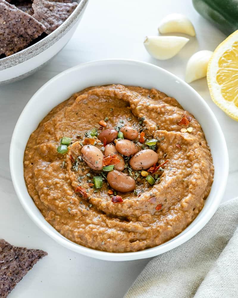 Gewürzter Bohnen-Dip 5 completed Spiced Refried Bean Dip in a bowl against a white background with ingredients spread in the back