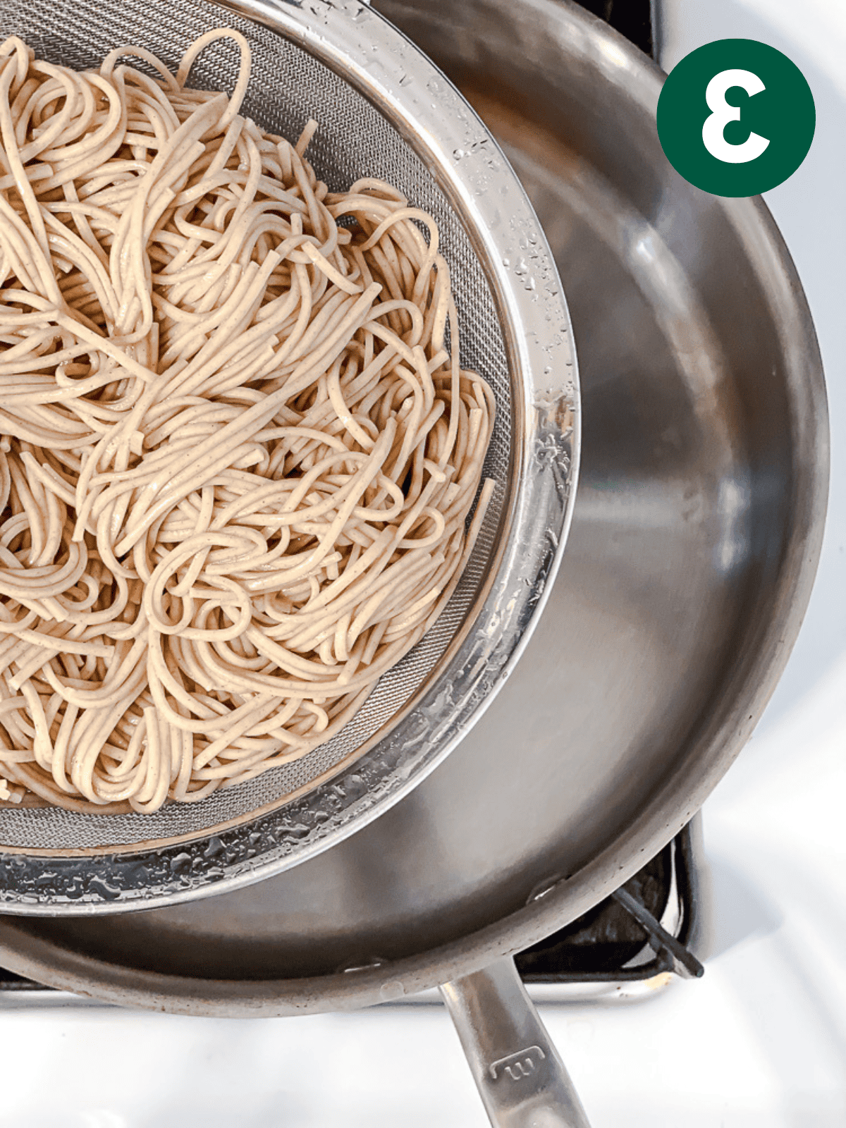 draining cooked soba noodles in a metal colander.