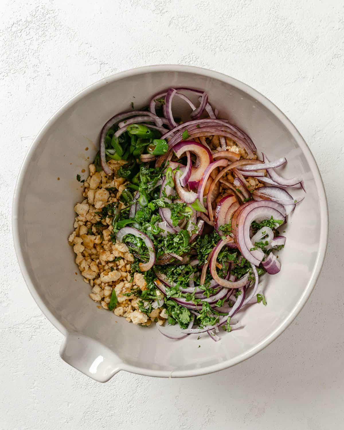 Veganer Tofu-Larb-Salat 6 Zutaten für Larb Salat in einer weißen Schale auf weißem Hintergrund.