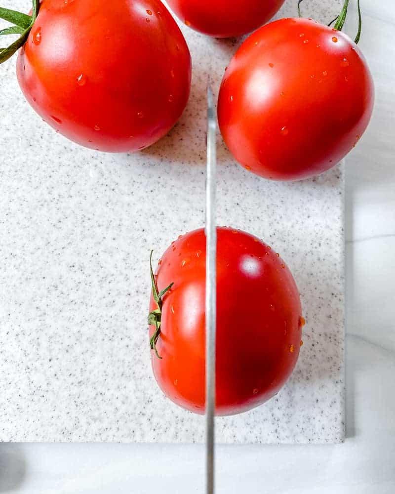 Gefüllte Tomaten 6 Prozessaufnahme: Eine Tomate auf einem weißen Schneidebrett schneiden