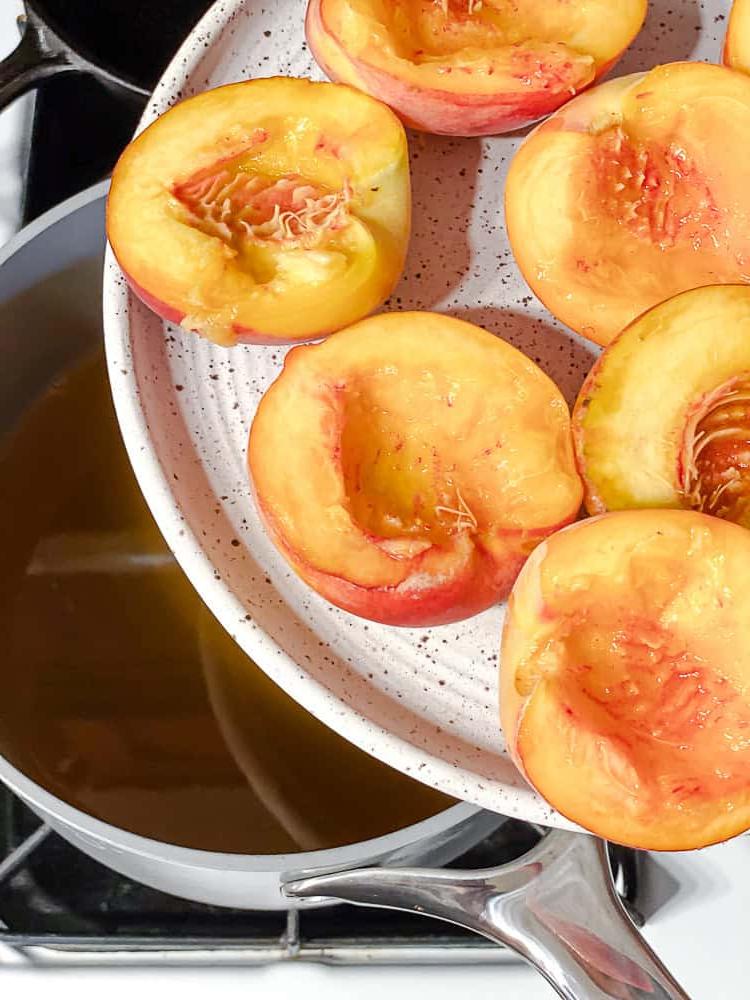 Peach Melba 6 Ein Teller mit Pfirsichen steht über einem Topf mit Zuckersirup bereit.