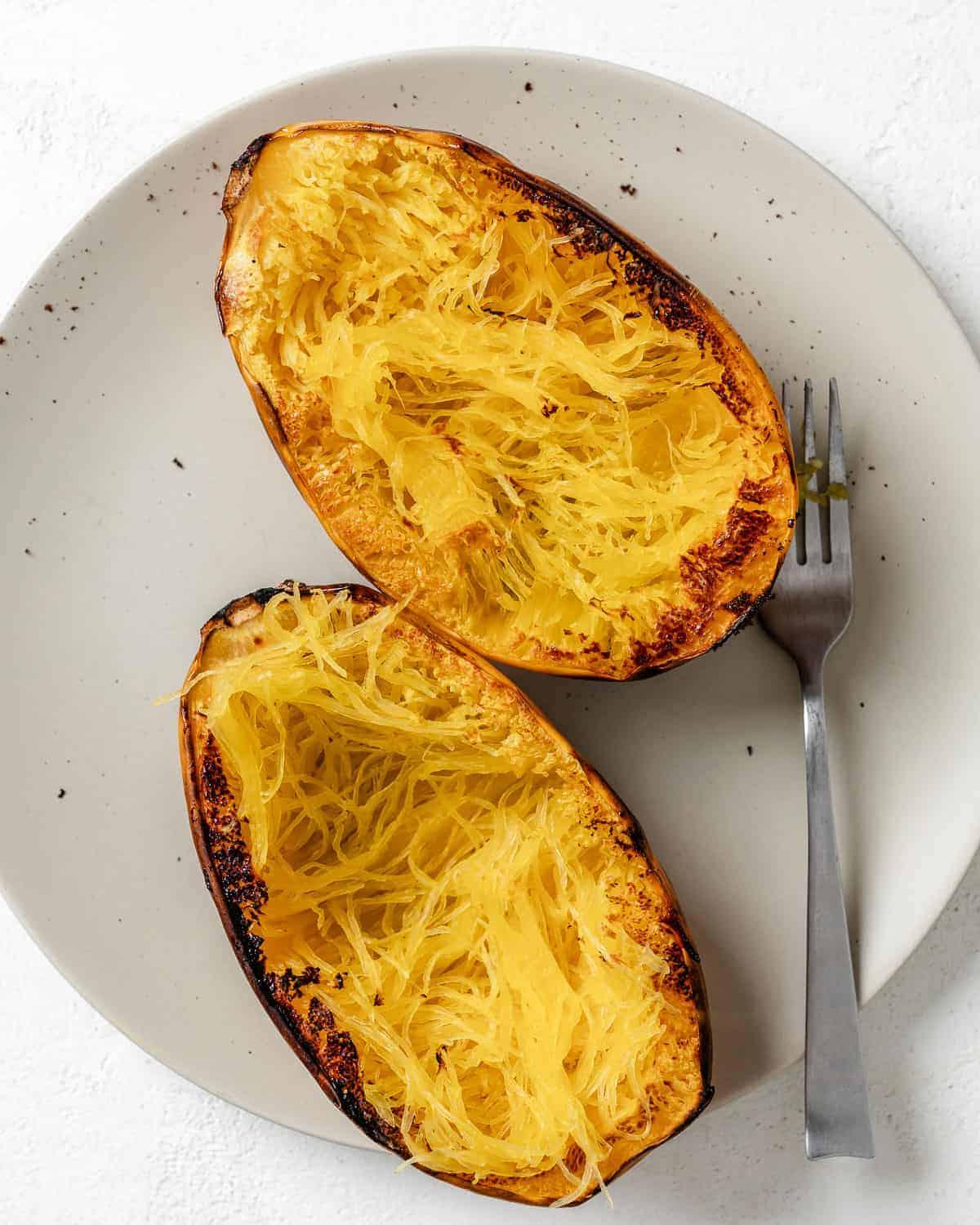 Chili-Käse-gefüllter Spaghettikürbis 6 cooked spaghetti squash halves on a white plate