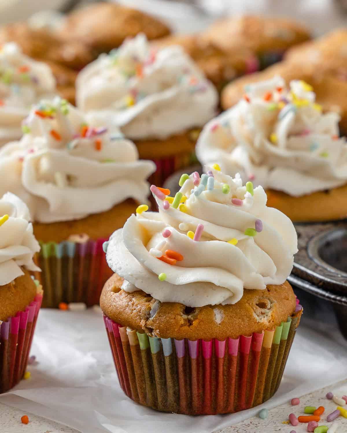 Vegane Konfetti-Cupcakes 6 Fertige vegane Funfetti Cupcakes auf einer weißen Oberfläche und in einer Muffinform, Nahaufnahme
