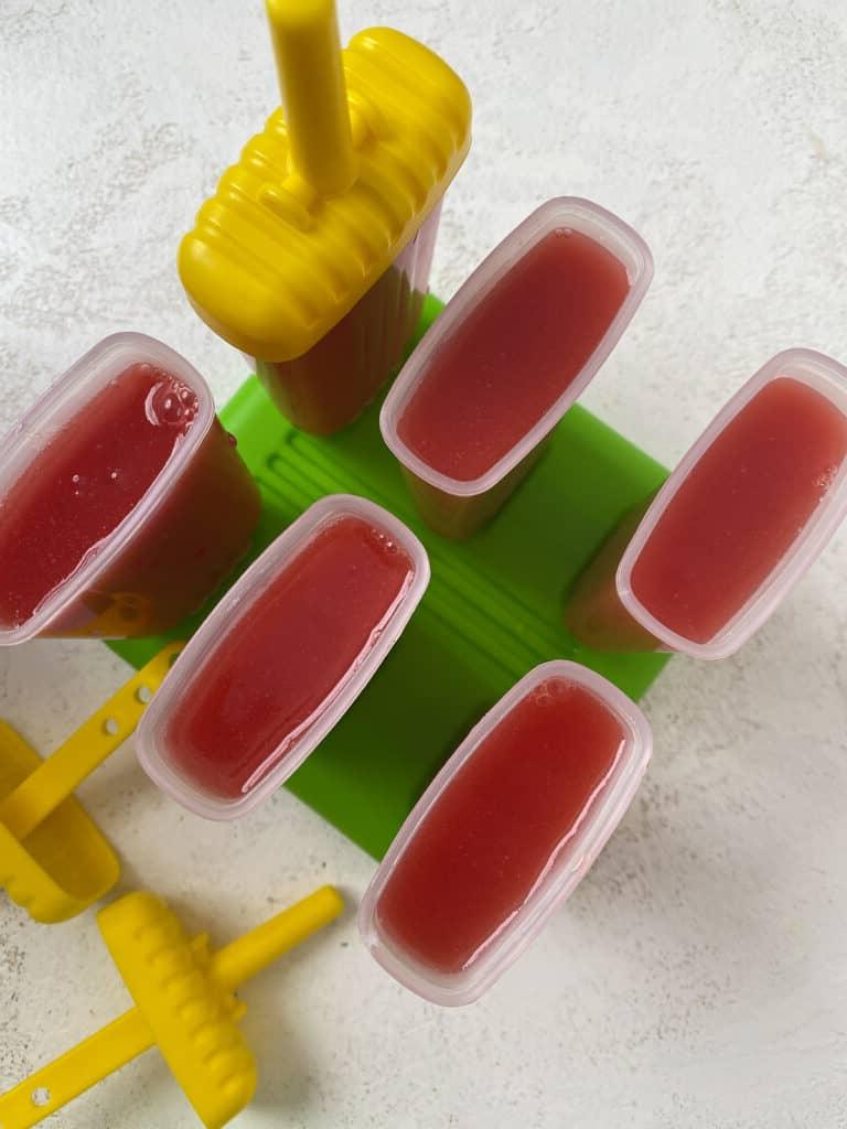 Gesundes Wassermelonen-Stieleis 6 Sechs Wassermelonen-Eis am Stiel in ihren Förmchen vor hellem Hintergrund