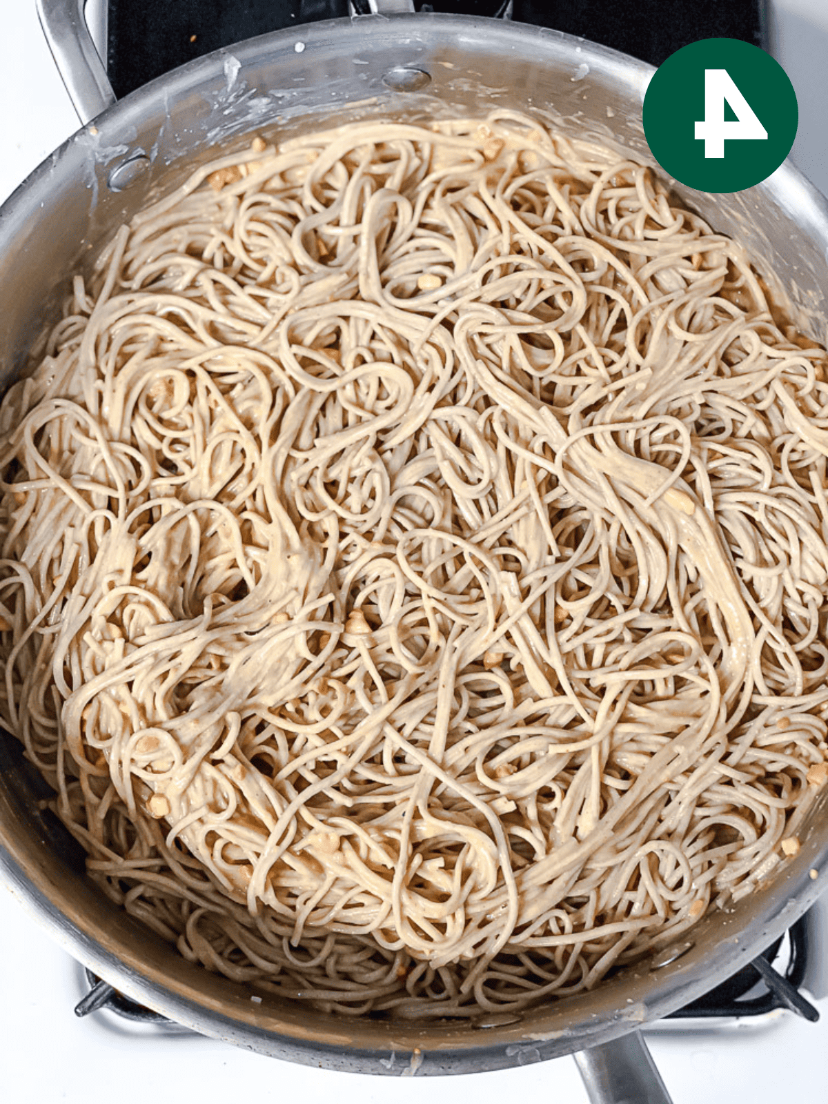 cooked soba noodles tossed in peanut sauce in a large metal poopt.