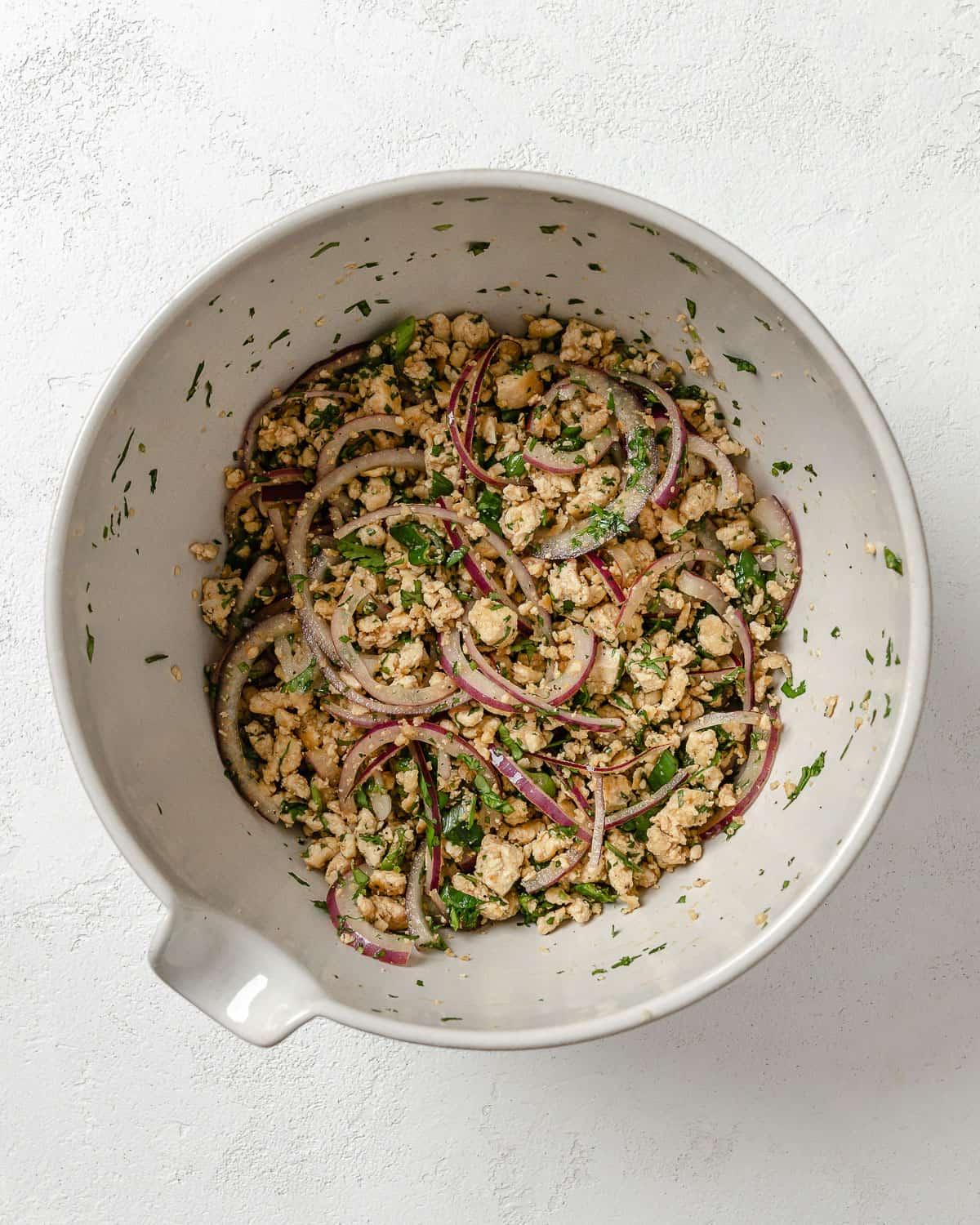 Veganer Tofu-Larb-Salat 7 Nach dem Mischen der Larb Salat Zutaten in einer weißen Schale auf weißem Hintergrund.