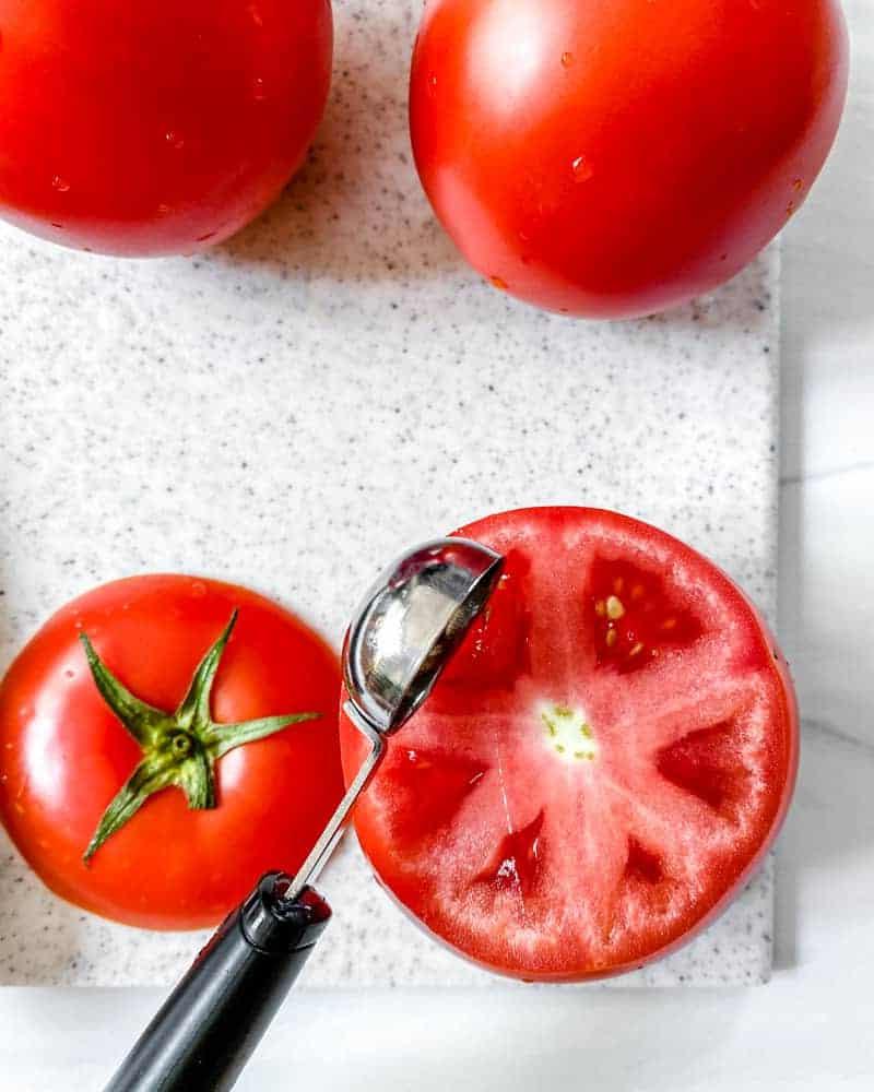 Gefüllte Tomaten 7 Prozessaufnahme: Das Innere einer Tomate auf einem weißen Schneidebrett aushöhlen