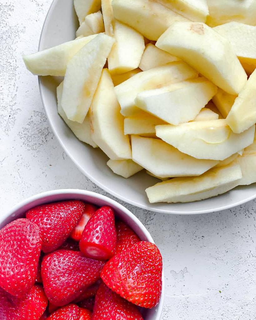Einfaches Erdbeer-Apfelmus 7 Geschnittene Äpfel und Erdbeeren in einer weißen Schüssel vor weißem Hintergrund