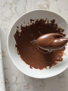 Vegane Schoko-Erdnussbutter-Kugeln ohne Backen mit Reis-Crispies 7 Prozess des Schmelzens von Schokolade in einer kleinen weißen Schüssel auf einer weißen Marmoroberfläche