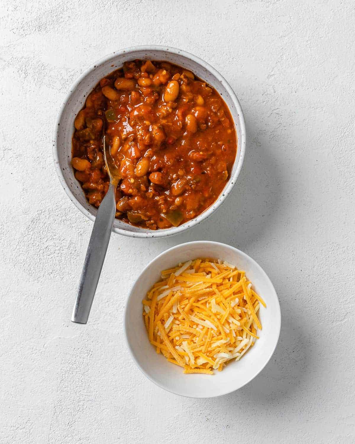 Chili-Käse-gefüllter Spaghettikürbis 7 ingredients for spaghetti squash in two bowls against white surface