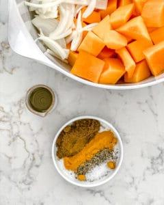 Zutaten für gerösteten Butternut-Kürbis mit indischen Gewürzen und karamelisierten Zwiebeln auf einer weißen Marmoroberfläche