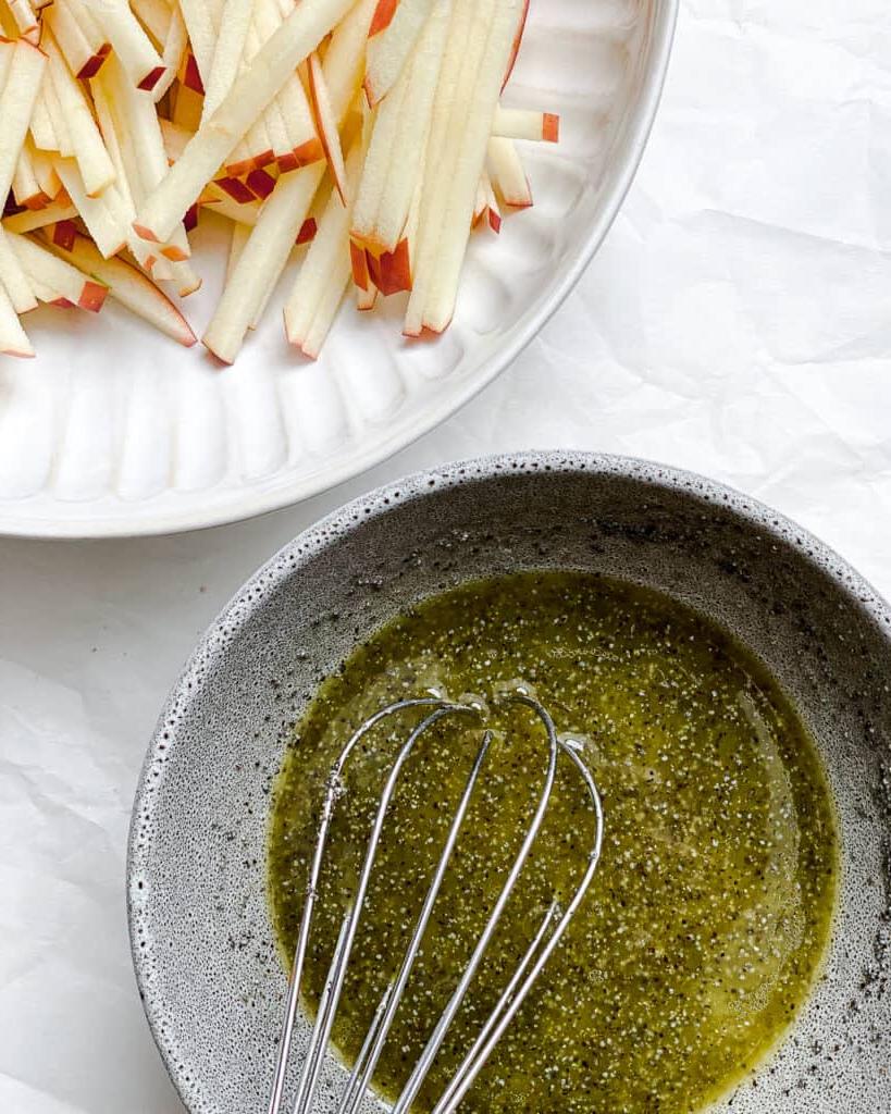 Gehobelter Rosenkohlsalat mit Äpfeln 7 Schüssel mit Dressing neben einer Schüssel mit Äpfeln