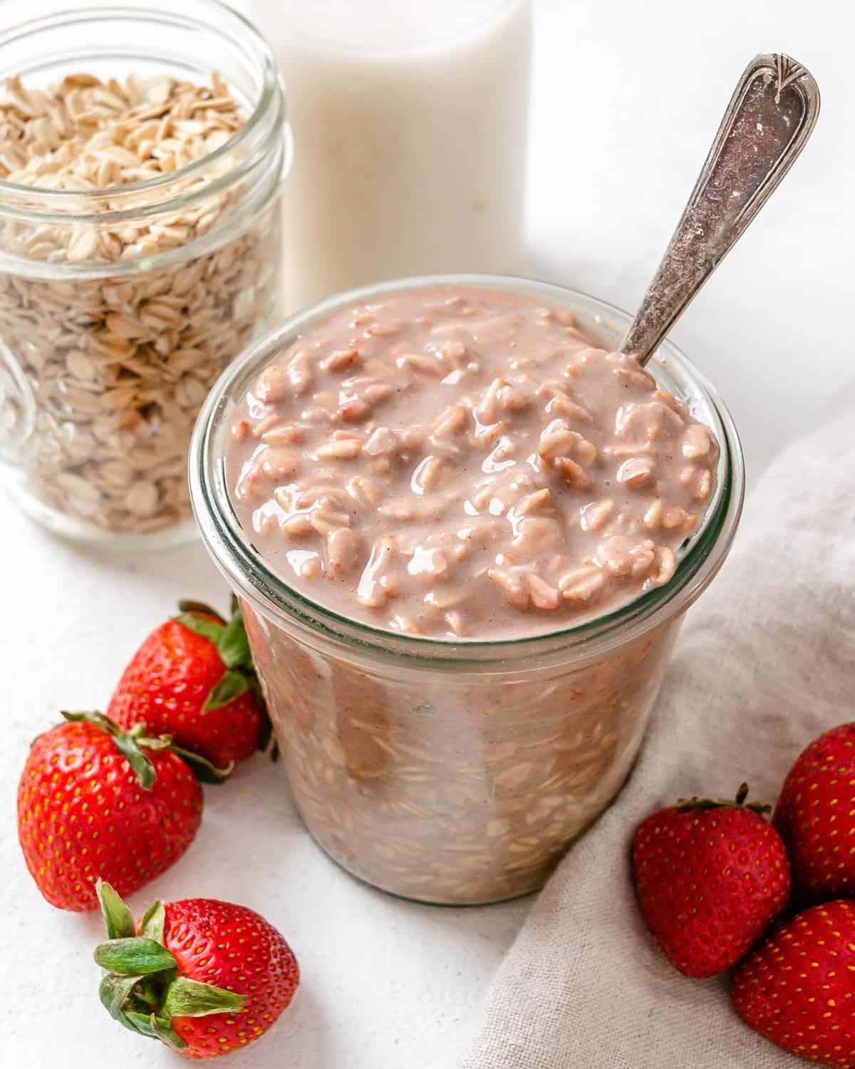 Erdbeer-Overnight-Oats (Vegan) 7 Fertige vegane Erdbeer Overnight Oats in zwei Gläsern mit Erdbeeren im Vordergrund auf einer weißen Oberfläche