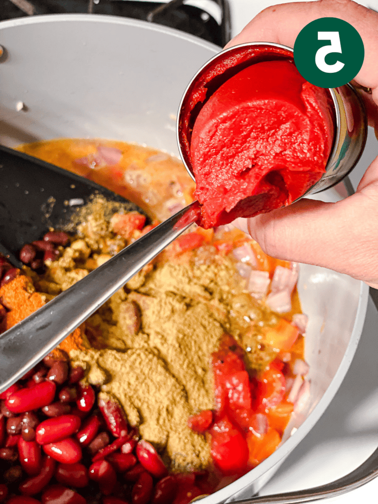 Veganes Kürbis-Chili für Schongarer und Herd 8 Prozessaufnahme des Hinzufügens von Tomatenmark zur Pfanne