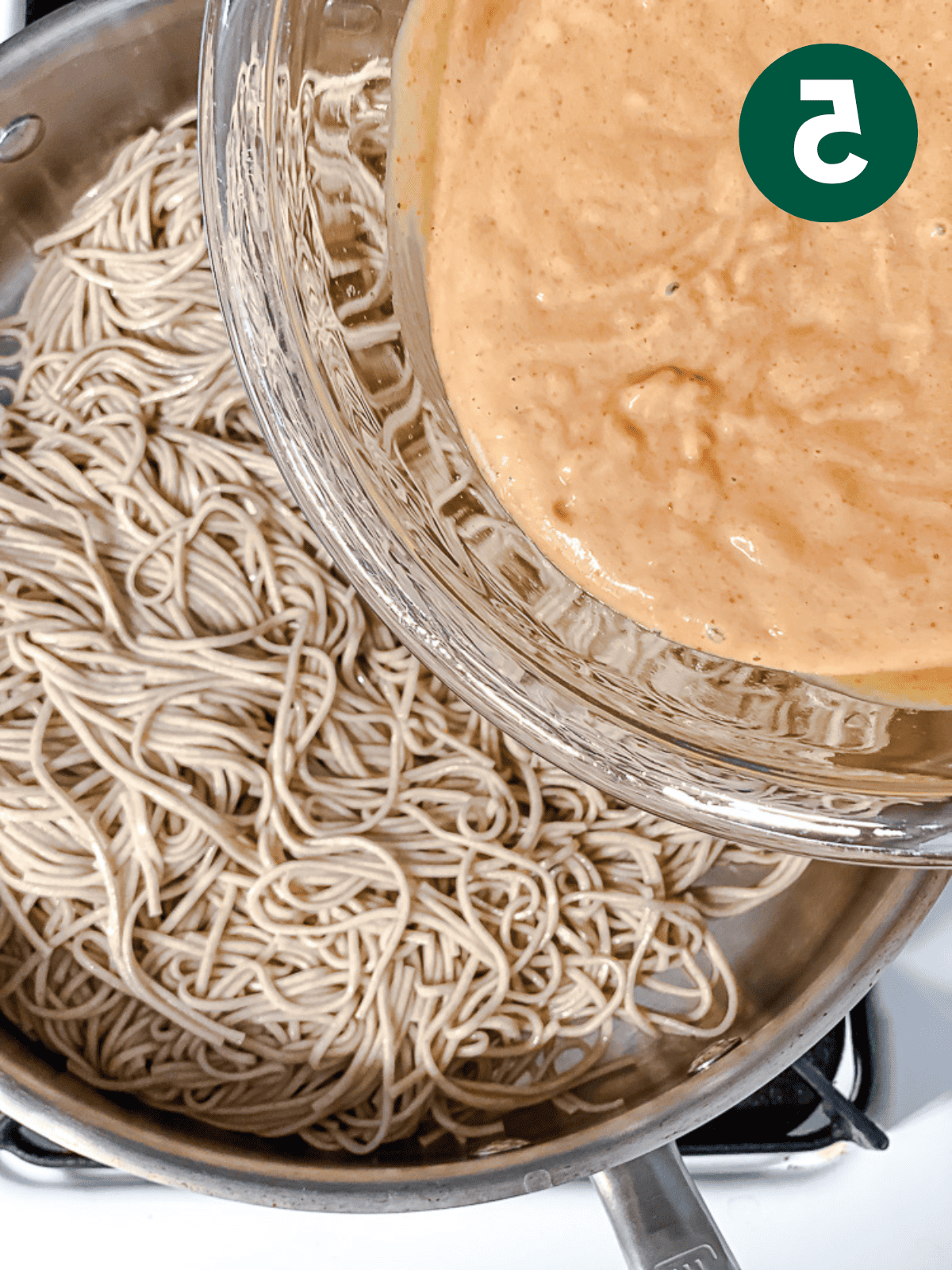 pouring peanut sauce over cooked soba noodles in a large pot.