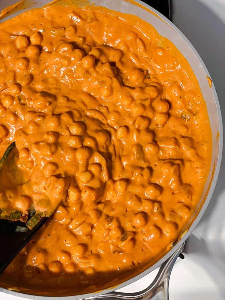 Curry-Kichererbsen 8 Prozessaufnahme: Kichererbsen-Curry wird mit einem schwarzen Löffel in einer großen Pfanne umgerührt.