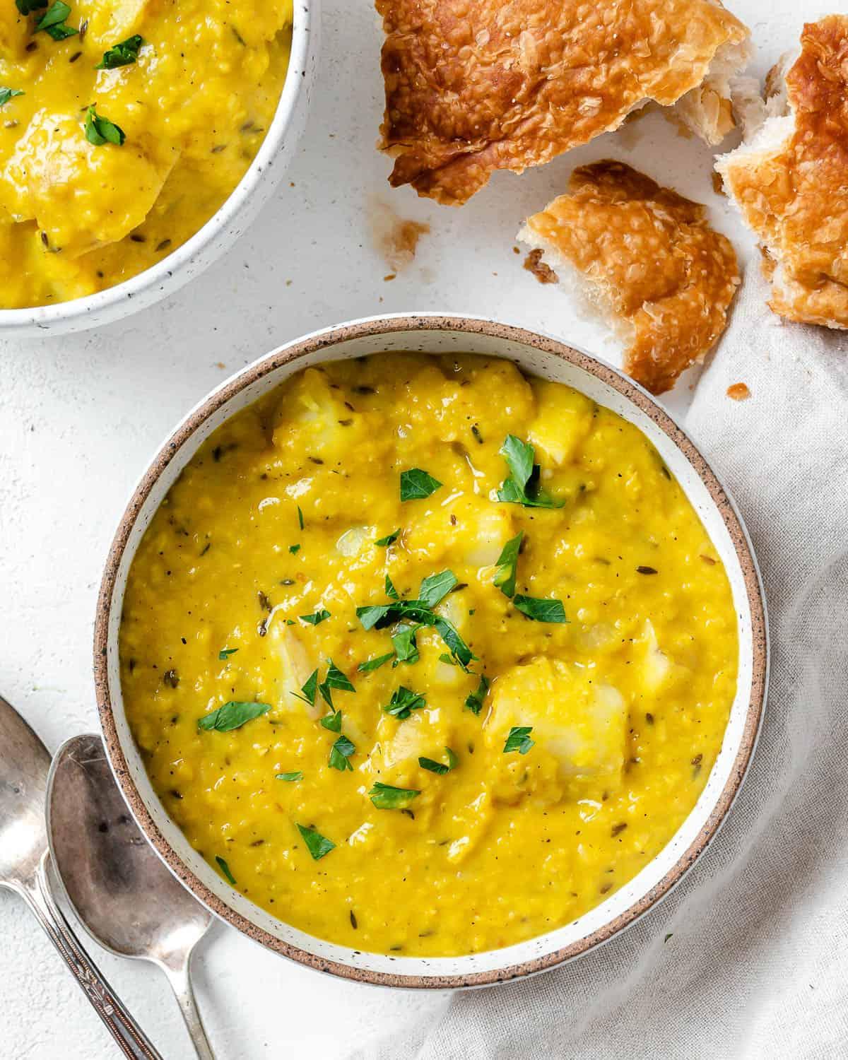 30 einfache vegane Kartoffelrezepte 8 Fertige Linsen-Kartoffel-Suppe in einer weißen Schüssel mit Zutaten im Hintergrund