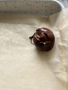 Vegane Schoko-Erdnussbutter-Kugeln ohne Backen mit Reis-Crispies 8 Prozess des Platzierens eines schokoladenüberzogenen Bonbons auf Backpapier
