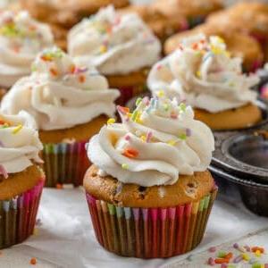 Vegane Konfetti-Cupcakes 8 Fertige vegane Funfetti Cupcakes auf einer weißen Oberfläche und in einer Muffinform