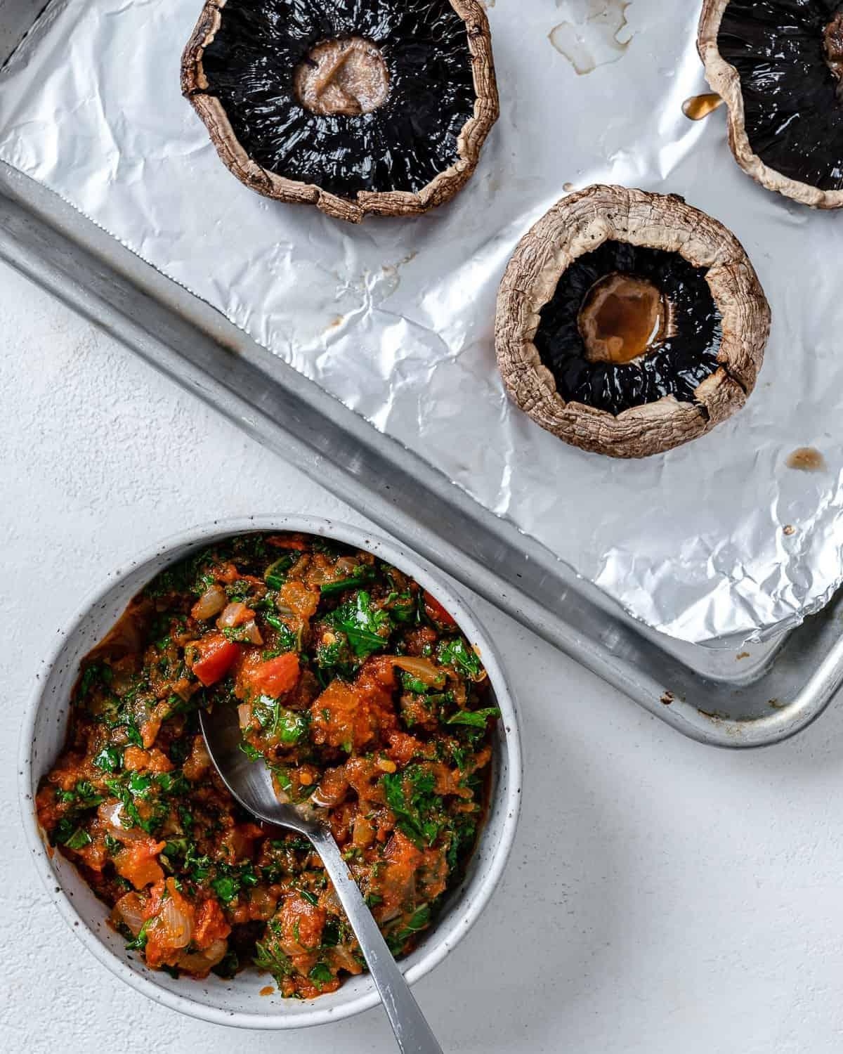 Portobello-Pilz-Pizzen 8 Pfanne mit Sauce neben Backblech mit Portobello-Pilzen vor weißem Hintergrund