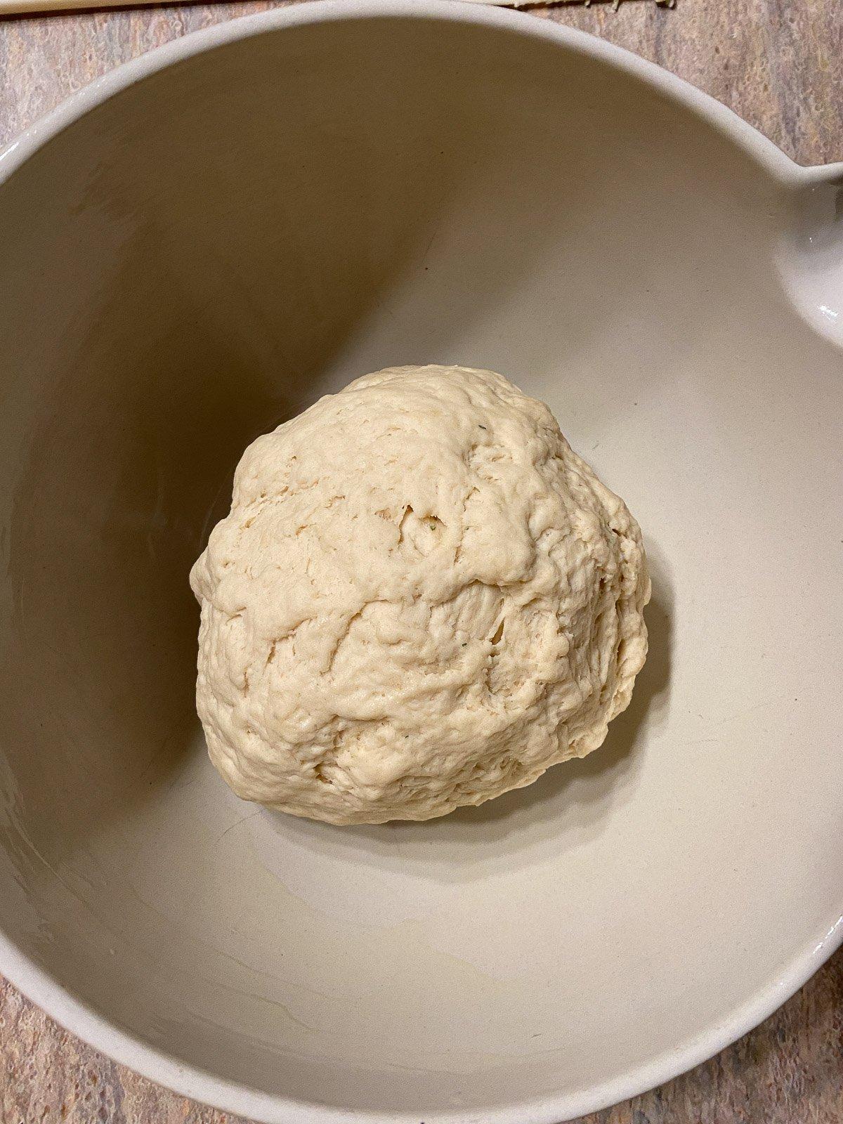 Vegane Pizzaröllchen 8 process of forming dough in a white bowl against a light brown surface