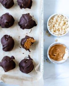 Vegane Schoko-Erdnussbutter-Kugeln ohne Backen mit Reis-Crispies 9 Mehrere fertige Erdnussbutter-Bonbons, eines davon mit einem Bissen