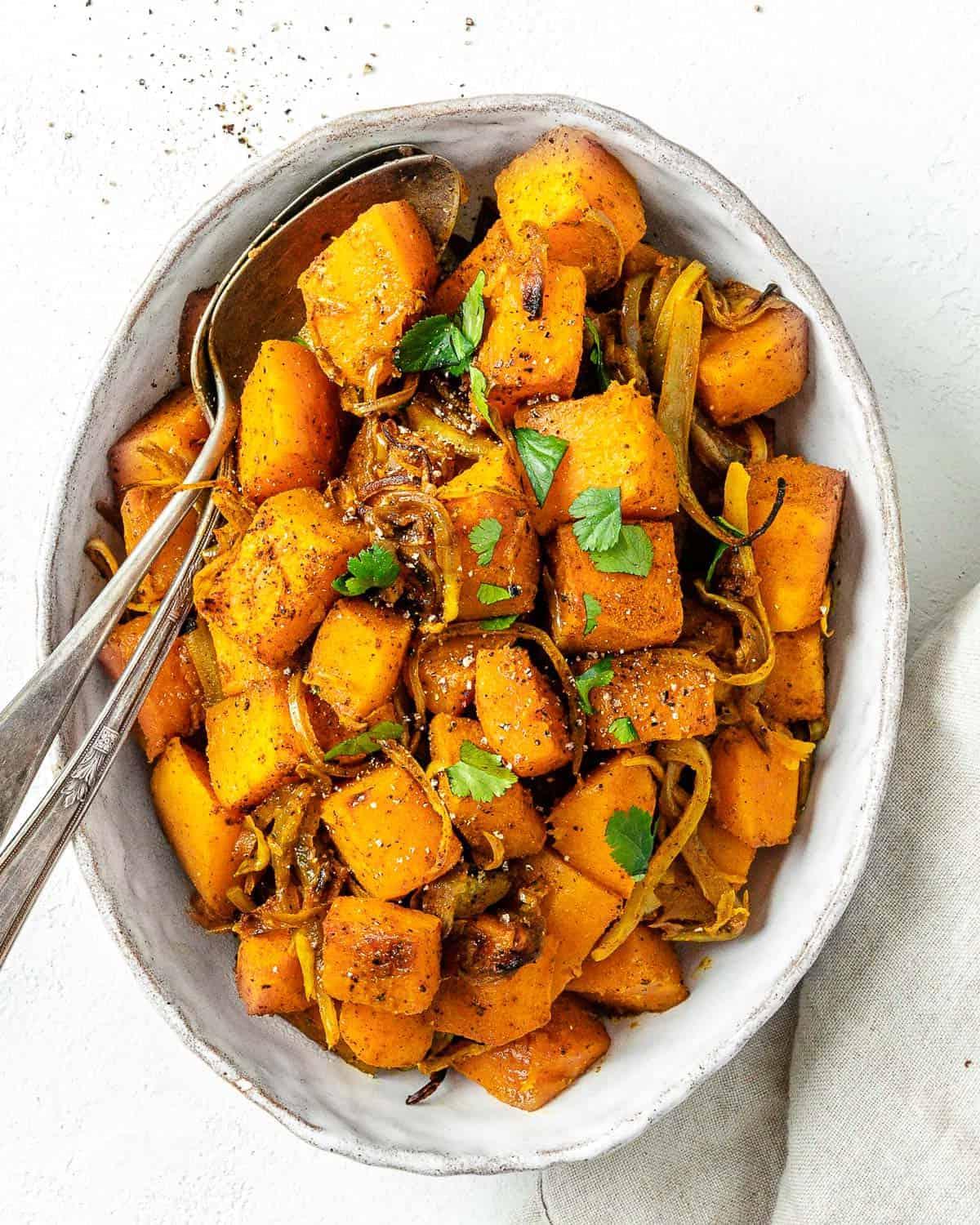 Fertig gerösteter Butternut-Kürbis mit indischen Gewürzen und karamelisierten Zwiebeln auf einer Servierplatte vor weißem Hintergrund