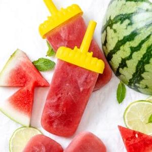 Gesundes Wassermelonen-Stieleis 9 Vier fertige Wassermelonen-Eis am Stiel mit Wassermelonenstücken im Hintergrund