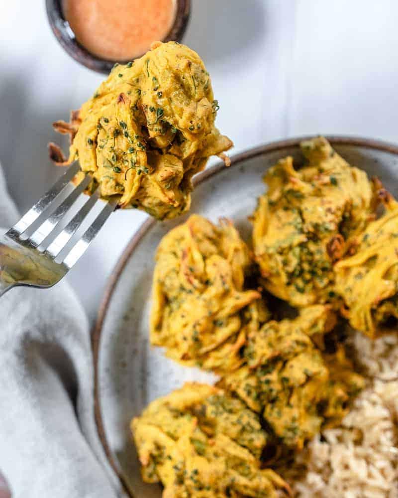 Fertige Brokkoli- und Zwiebel-Pakora auf einem Teller mit einer Nahaufnahme eines Stücks, das mit einer Gabel aufgenommen wird
