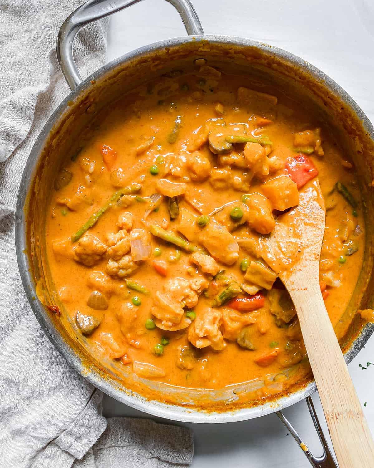 Fertiges Butternut-Kürbis-Curry im Topf mit Holzlöffel auf hellem Hintergrund