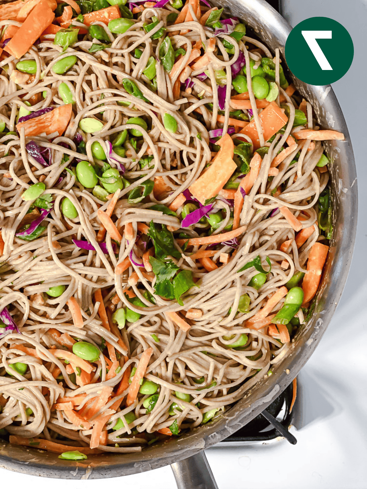 soba noodle salad tossed with peanut sauce and vegetables in a large pot.