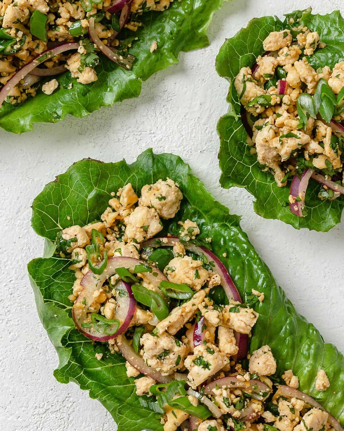 Veganer Tofu-Larb-Salat 10 Drei Portionen Larb Salat auf weißer Oberfläche angerichtet.