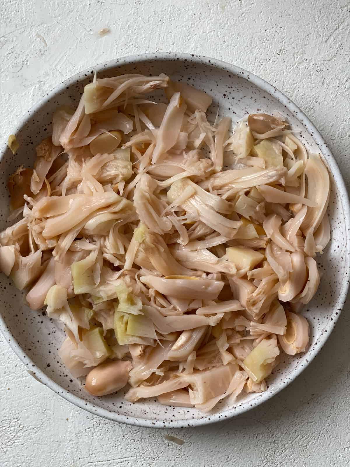 Jackfrucht-Salatwickel 10 Zerkleinerte Jackfrucht auf einem weiß gesprenkelten Teller