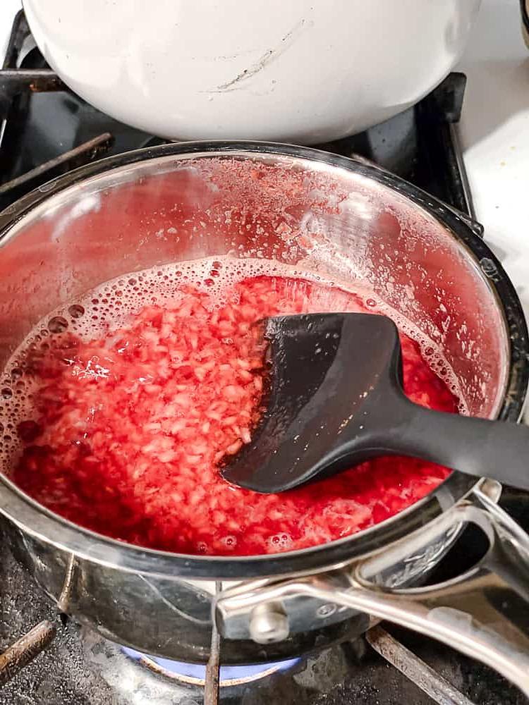 Peach Melba 10 Ein schwarzer Spatel rührt Himbeersauce in einem Topf.
