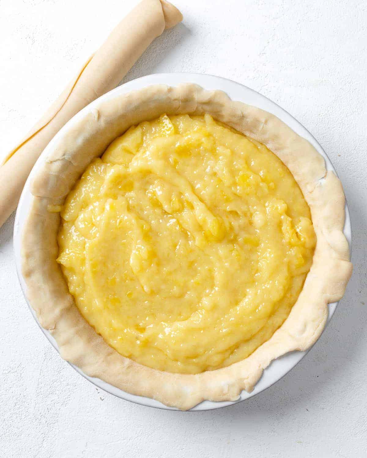 Veganer Kokos-Ananas-Kuchen 10 Arbeitsschritt: Ananasfüllung in Kuchenform geben vor weißem Hintergrund