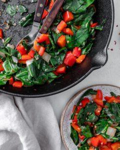 Scharfer Blattkohl 10 completed Spicy Collard Greens in a black pan against a white surface with a serving in a clear container on the side
