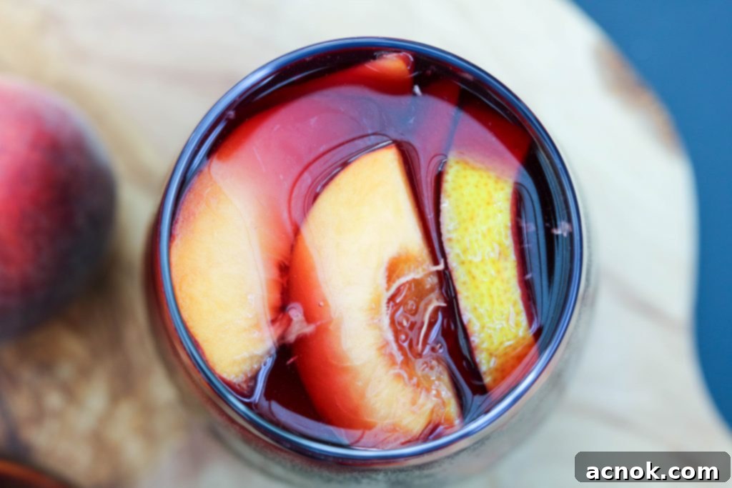 Top-down view of a pitcher of sangria with sliced oranges, lemons, peaches, and plums, garnished with fresh mint.