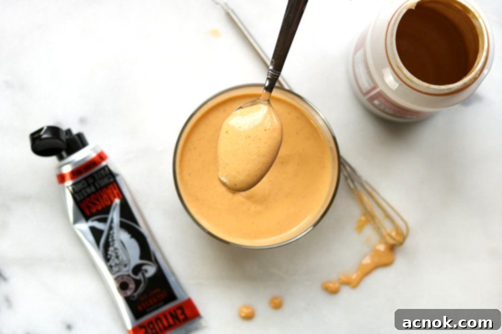 A spoonful of rich, golden Tahini Harissa Sauce being lifted from a bowl, showcasing its creamy texture and vibrant color.
