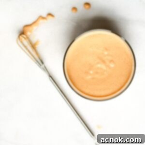 A bowl of Golden Tahini Harissa Sauce with a whisk resting next to it, indicating fresh preparation and readiness to serve.